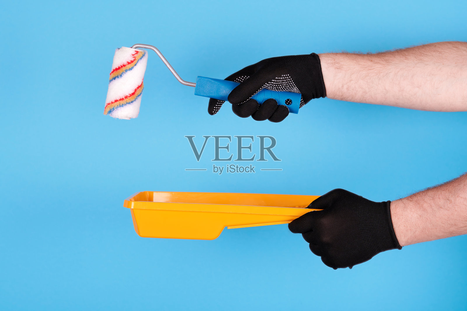 将工作手套与漆辊和塑料托盘交上。孤立在蓝色背景。照片摄影图片