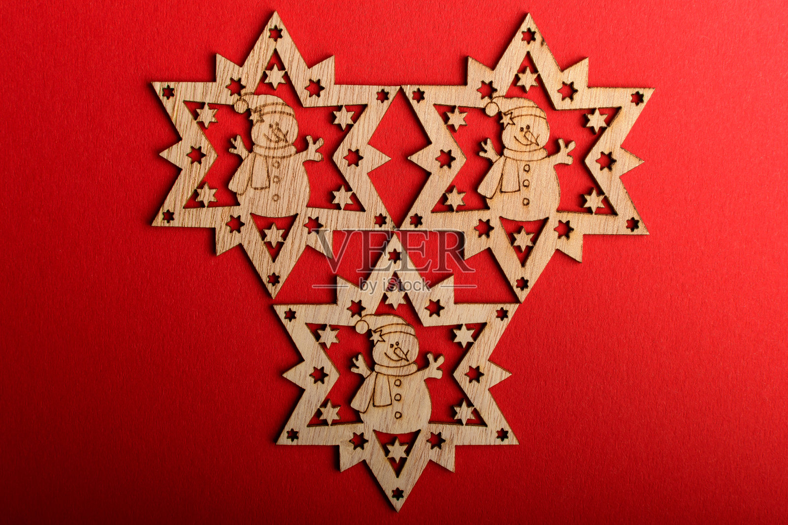 三个浅棕色的木制雪花在鲜艳的红色纹理纸板背景上，显示在左边和底部，顶部视图和右边的文字空间，与激光切割的木制物体平躺照片摄影图片