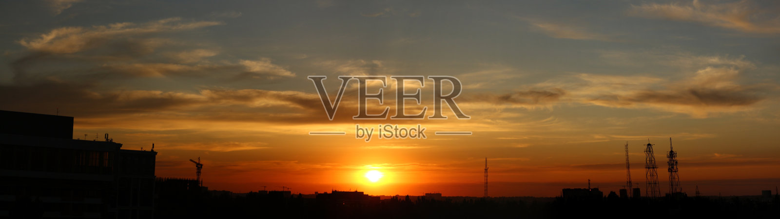 落日映衬下城市的彩色照片。黄色的太阳从地平线上落下。天空中美丽的云彩。从蓝色到红色的平滑自然渐变。一天结束。照片摄影图片