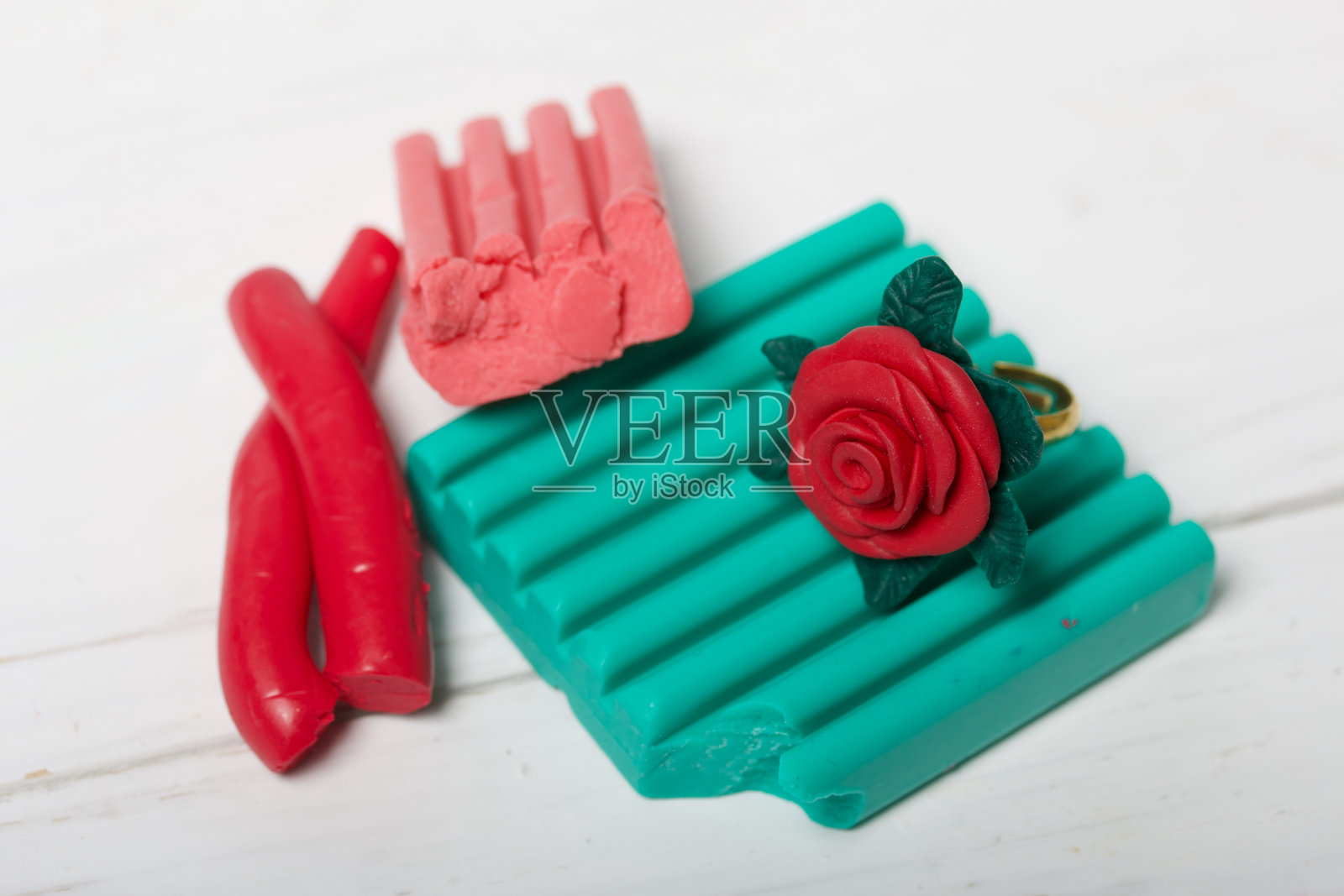 手工戒指装饰聚合物粘土玫瑰。旁边是一片片不同颜色的软陶。软陶做的珠宝。照片摄影图片