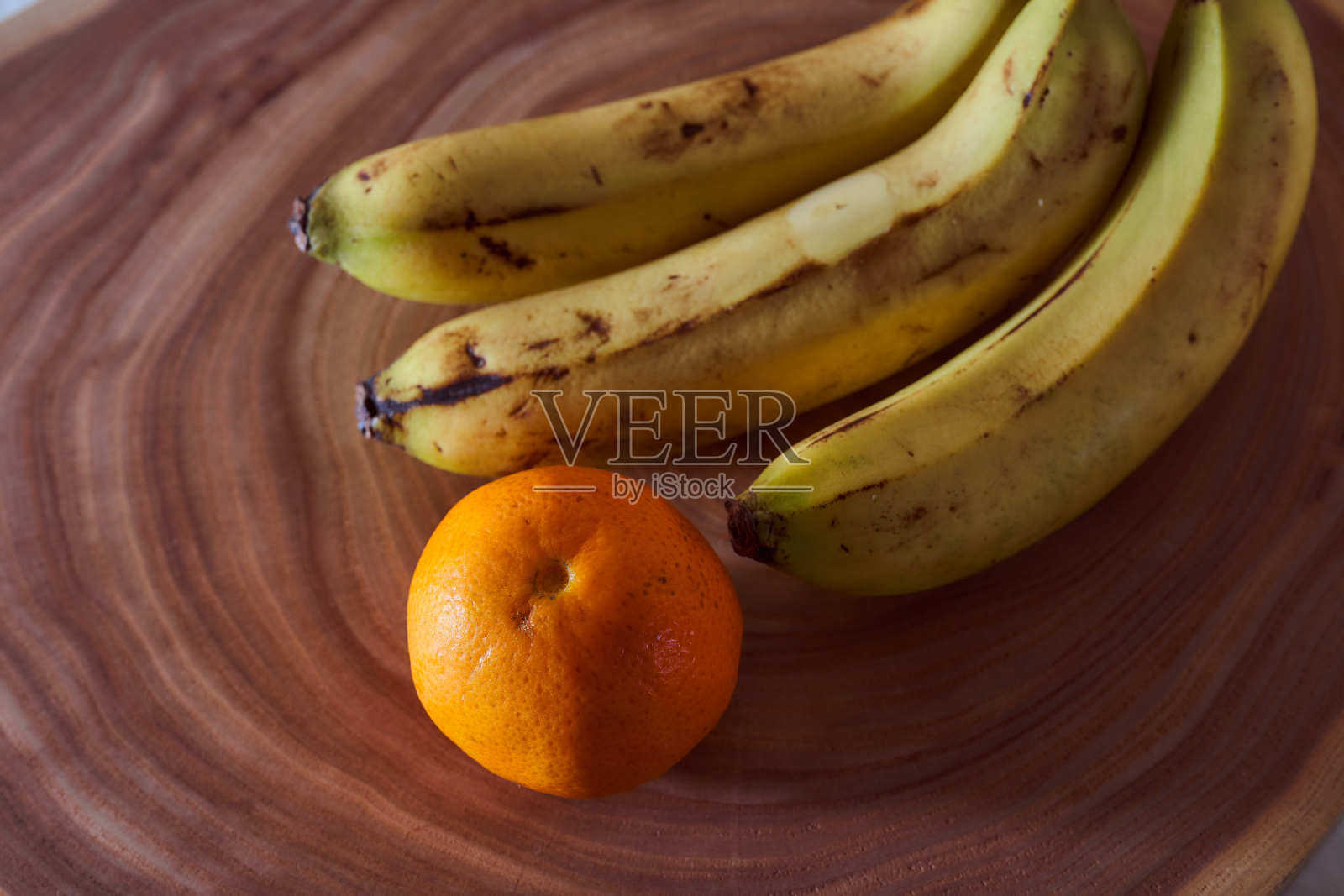 一根黄香蕉和桔子躺在一片树上。木制背景照片摄影图片