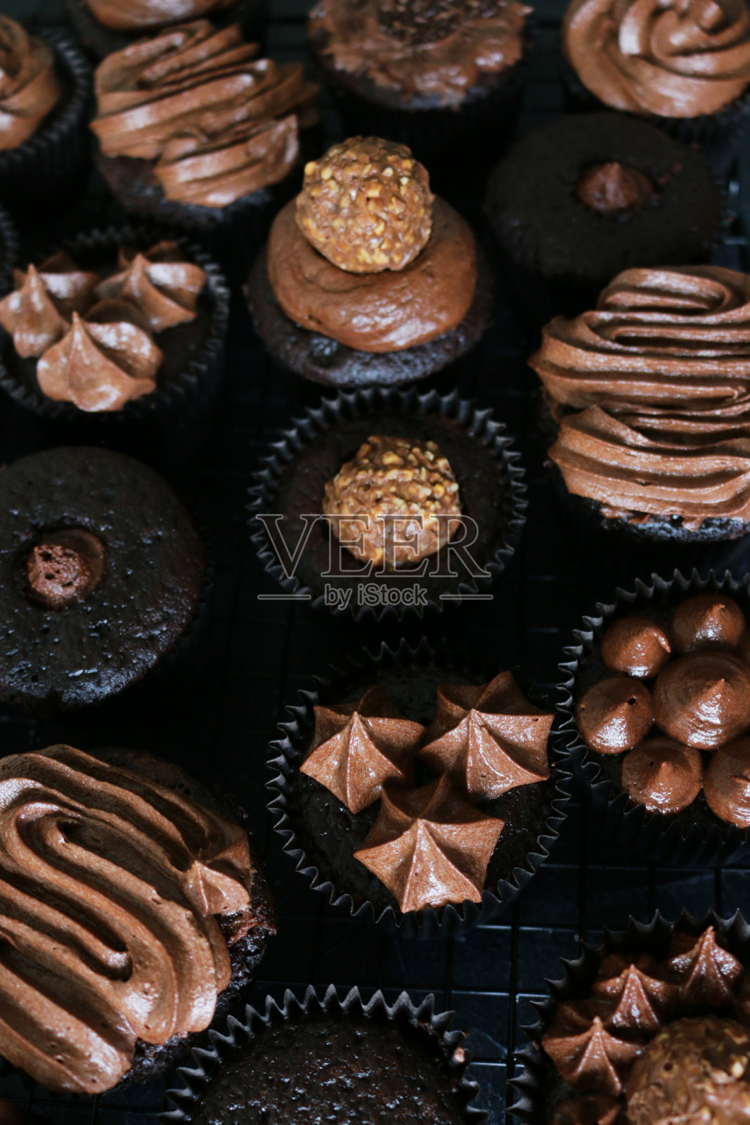这是自制巧克力纸杯蛋糕的特写，上面覆盖着管道状的巧克力糖霜，黑色的纸蛋糕盒放在金属冷却架上，居高临下的视野照片摄影图片