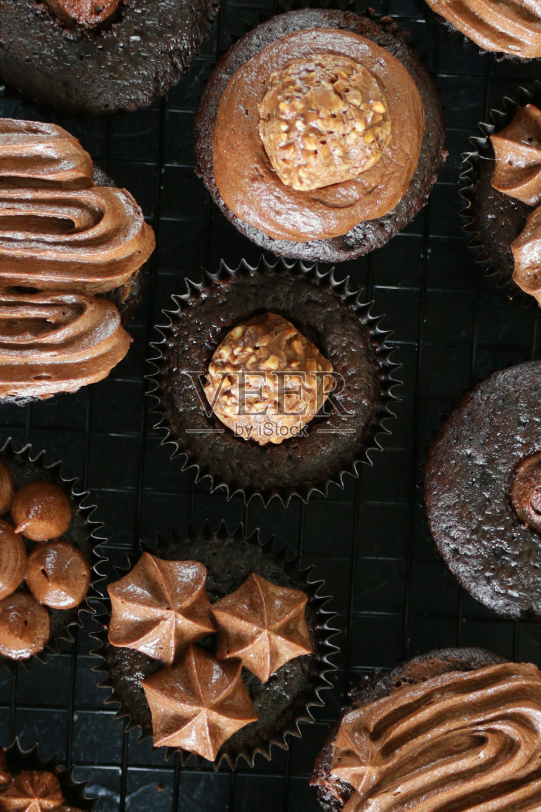 这是自制巧克力纸杯蛋糕的特写，上面覆盖着管道状的巧克力糖霜，黑色的纸蛋糕盒放在金属冷却架上，居高临下的视野照片摄影图片