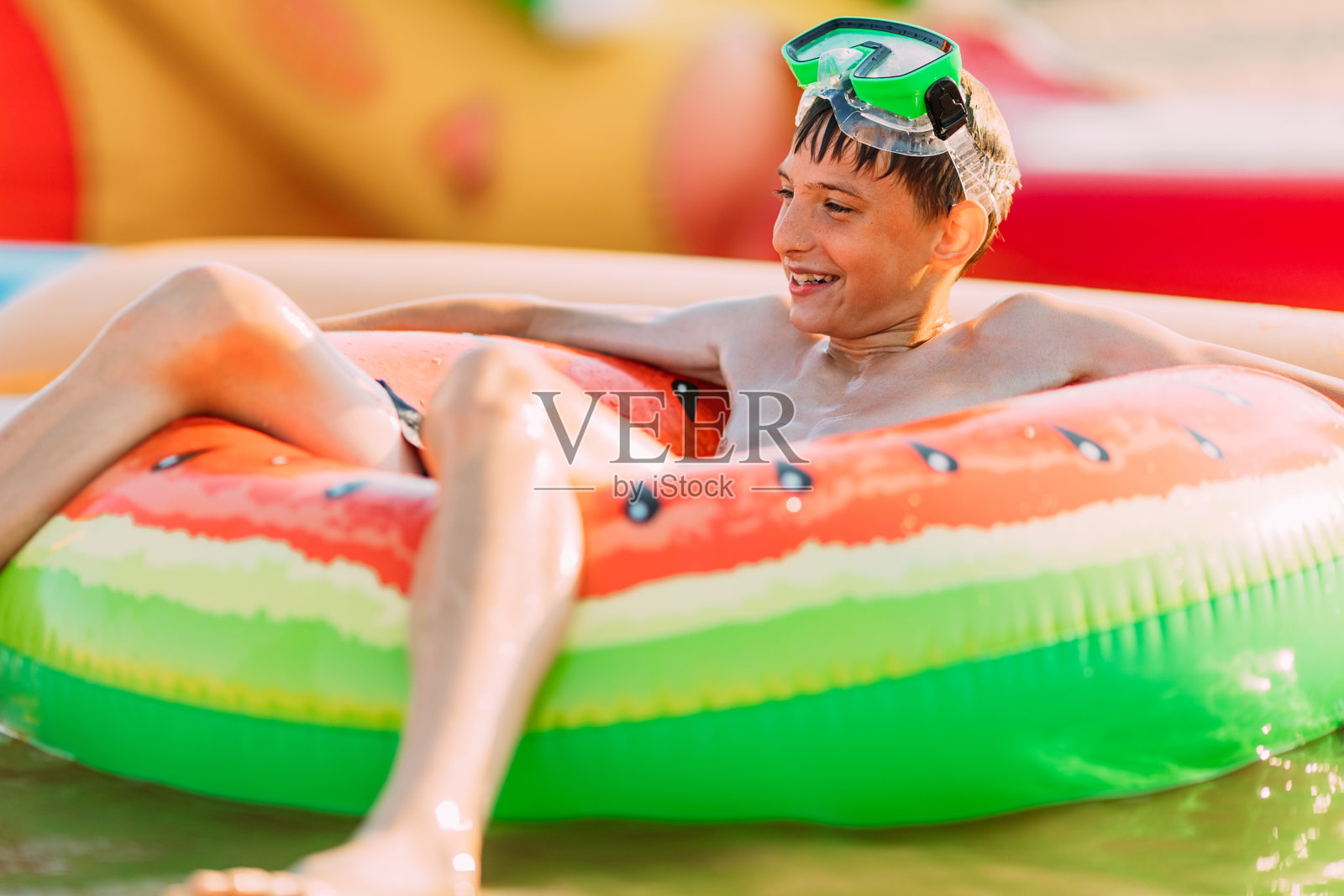 带着游泳眼镜的快乐微笑的少年躺在沙滩上，还有一个充气圈。暑假照片摄影图片