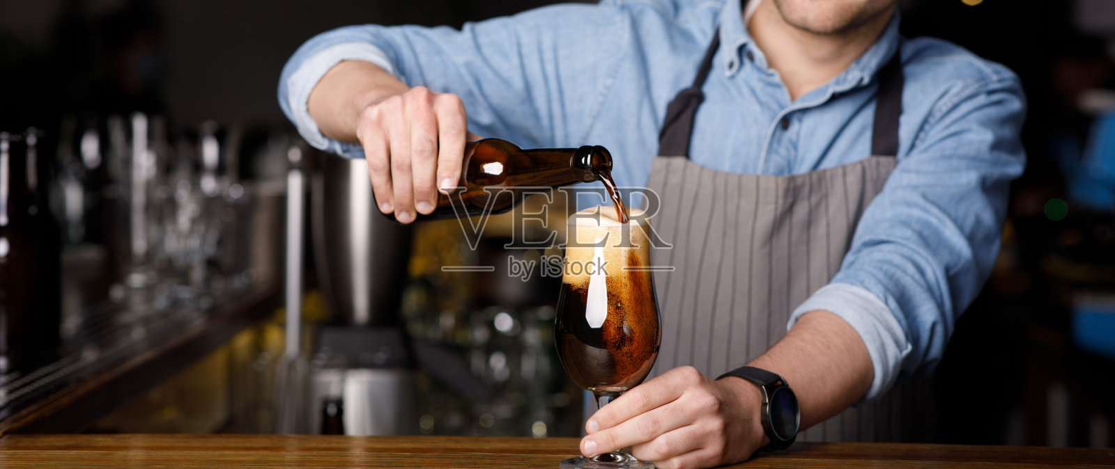 客户在酒吧点菜。酒吧侍者将黑啤酒倒入玻璃杯中照片摄影图片