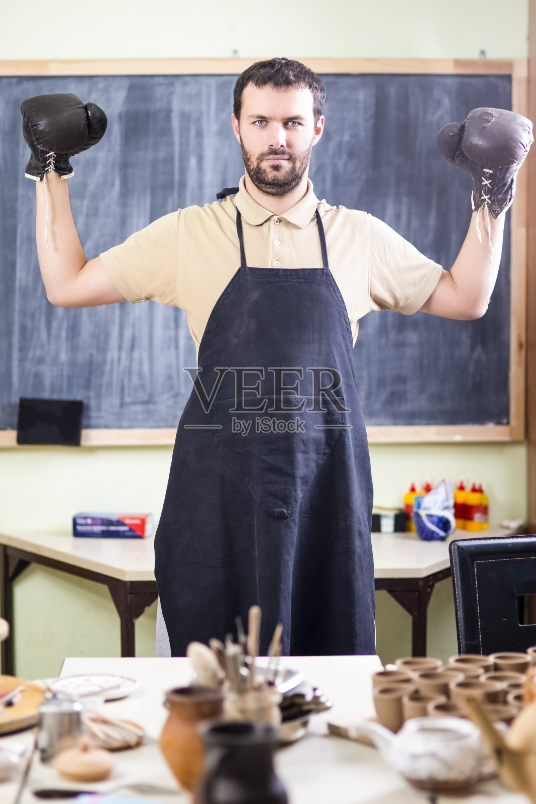 拳击手套专业男性陶艺家。在车间的防护围裙中摆姿势。垂直的图像组成照片摄影图片
