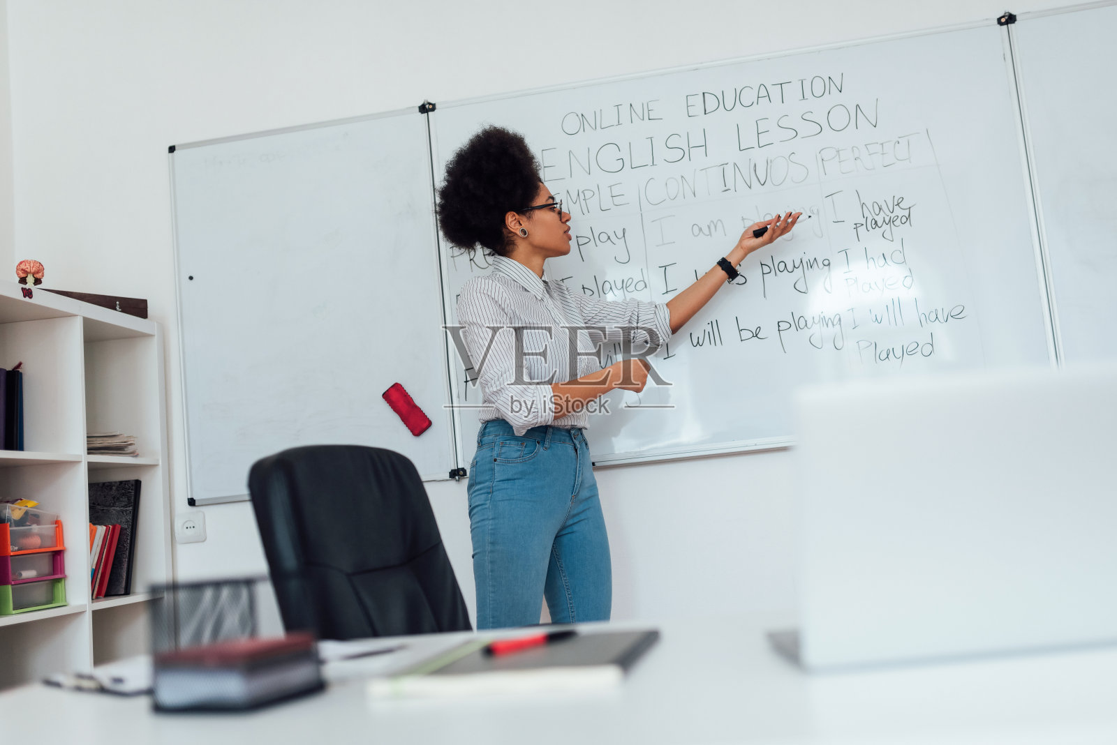 给在线课程。年轻的美国黑人女教师，穿着便服，站在白板旁讲解英语语法照片摄影图片