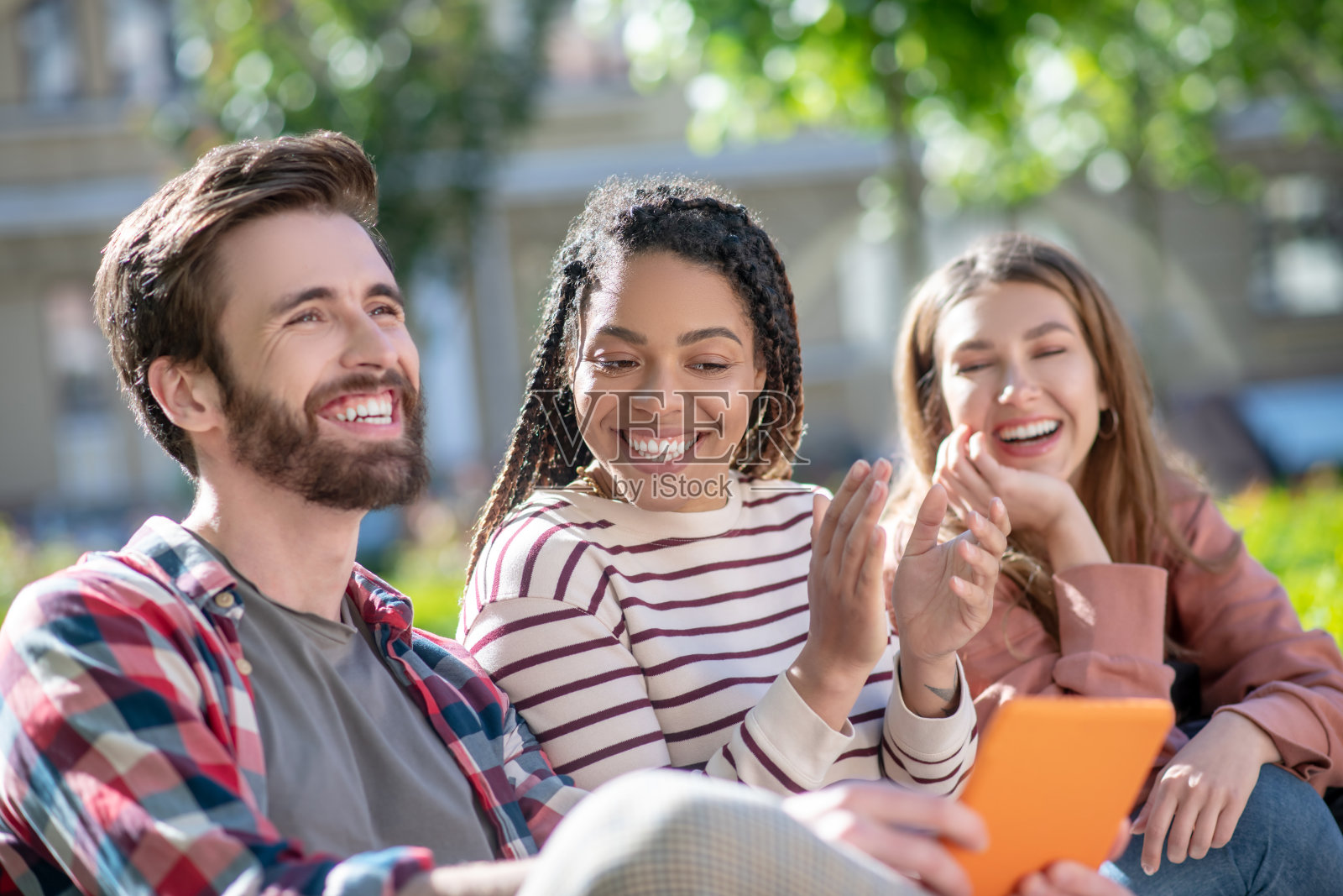 开心有趣的家伙，拿着平板电脑，还有两个坐在长椅上的女孩。照片摄影图片