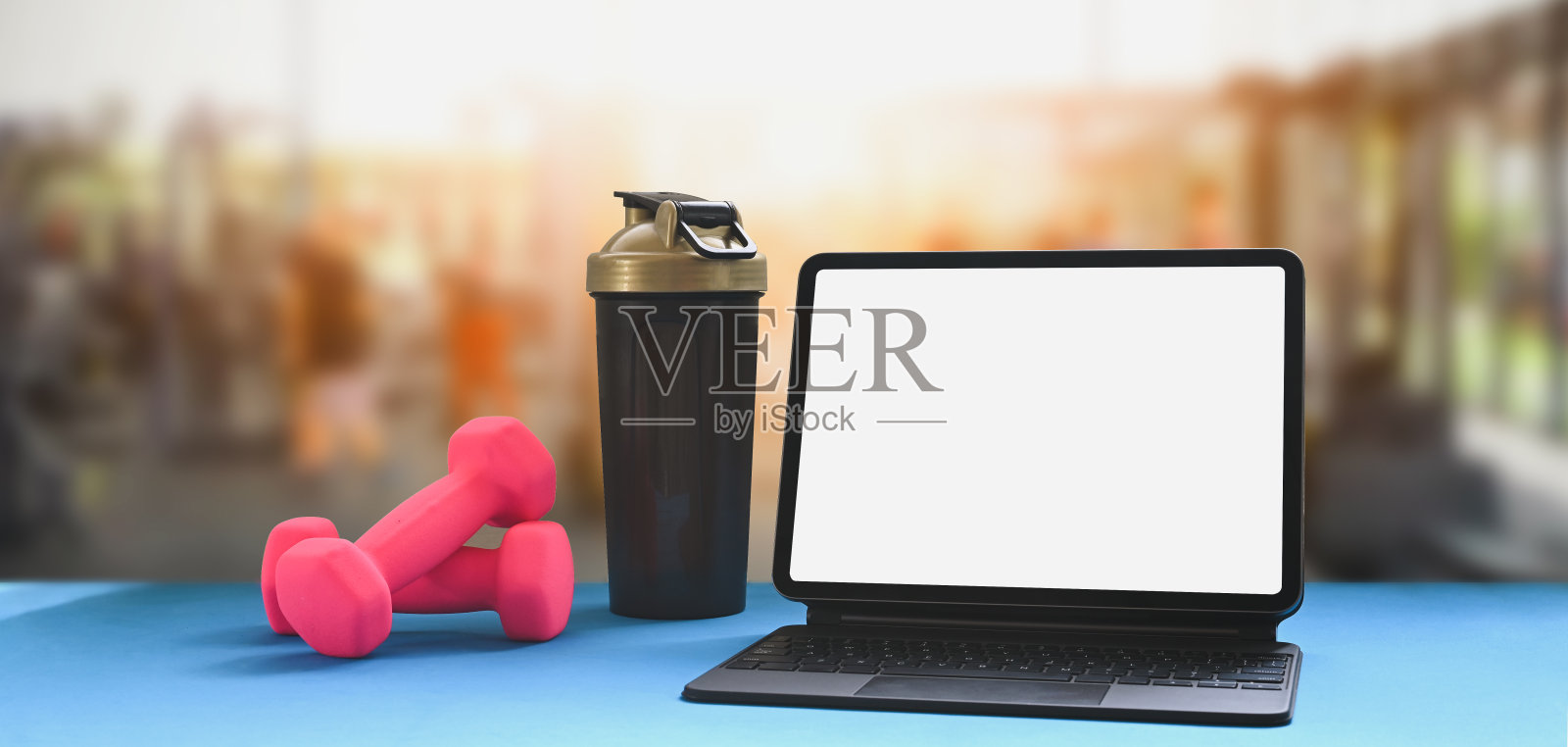 桌子上放着一台平板电脑，背景是一个模糊的体育馆。照片摄影图片