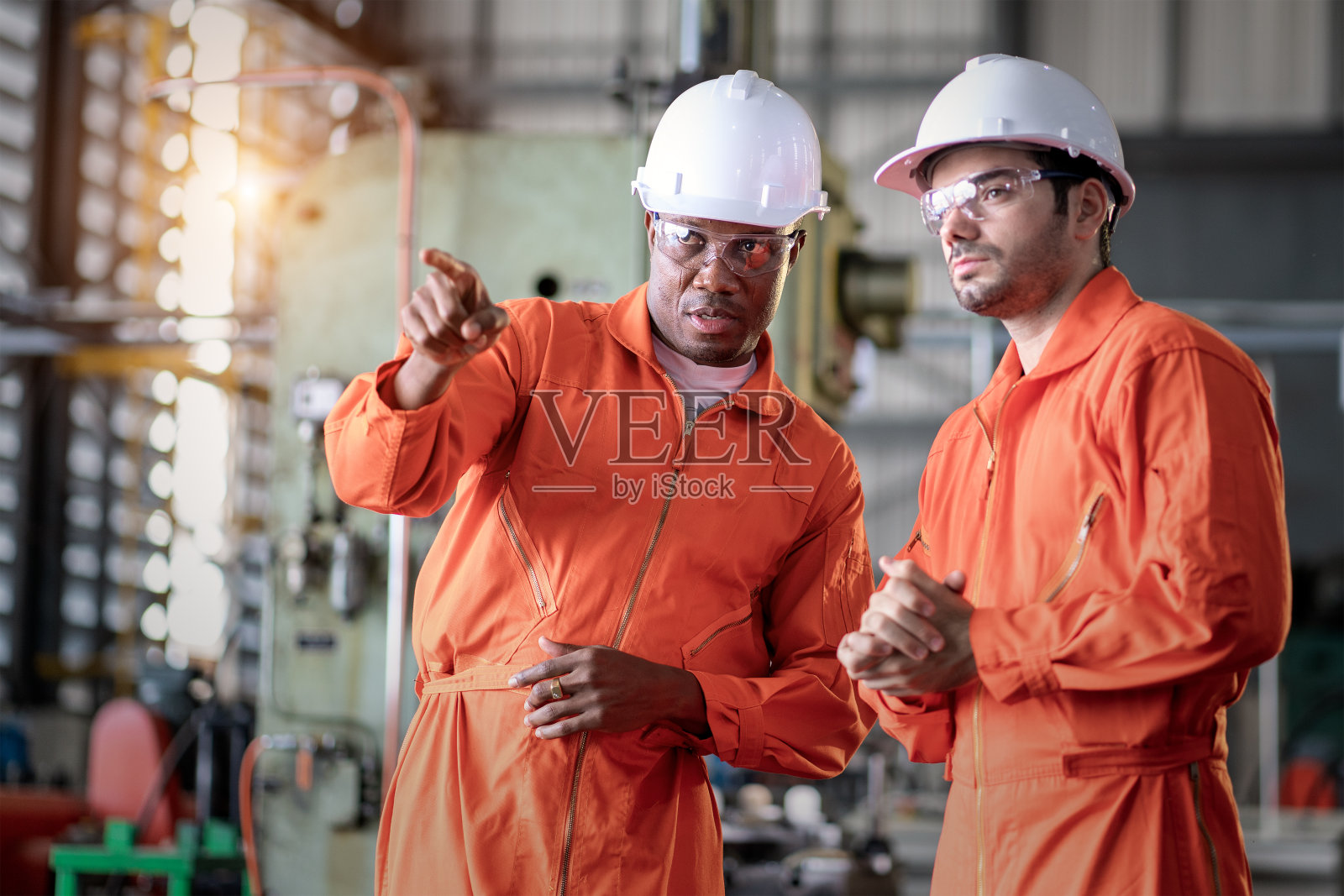 两位工程师戴着安全帽在工厂讨论新项目。照片摄影图片