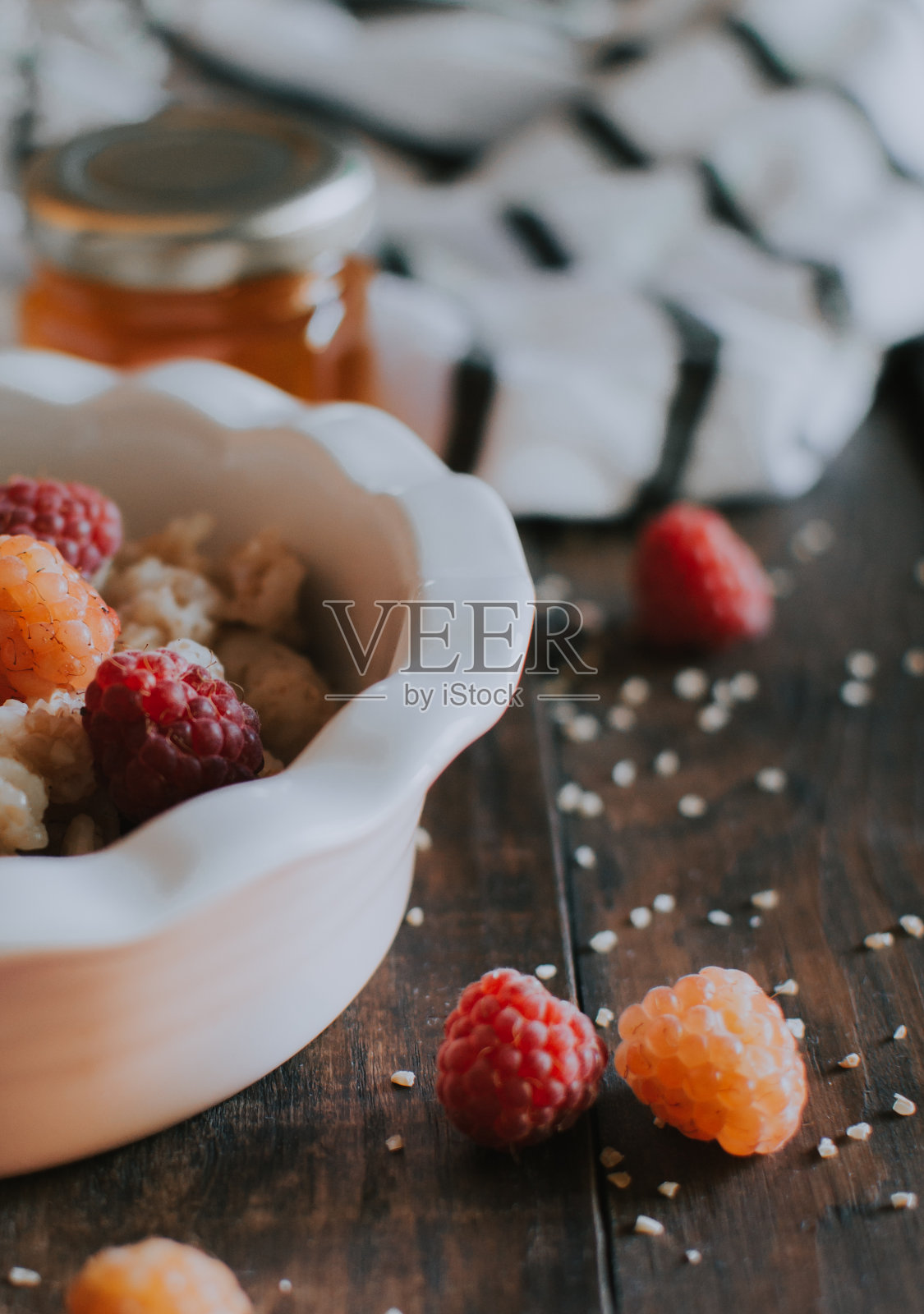 美味健康的早餐，有树莓和蜂蜜。早餐燕麦片。晨光美学和美丽的木桌布局。照片摄影图片