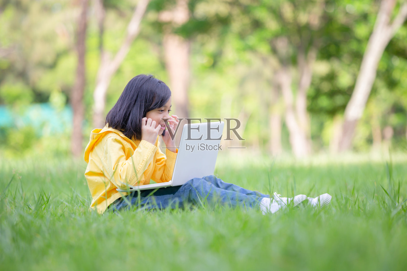 快乐的小女孩坐在草地上用笔记本电脑在公园里学习，户外学习概念照片摄影图片