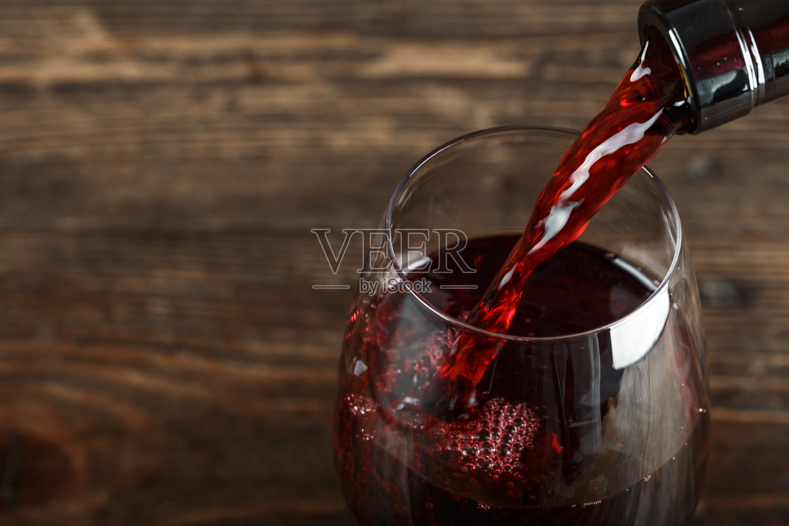 在玻璃杯中倒入红酒，在木背景上照片摄影图片
