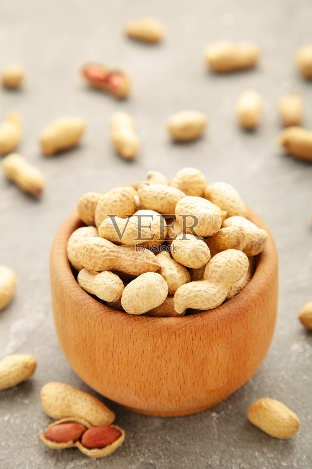 在灰色背景的木碗里的干花生。垂直与照片摄影图片