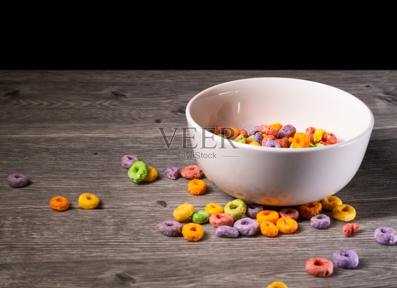 灰色的桌子上放着一只白色的碗，里面有许多彩色的麦片照片摄影图片