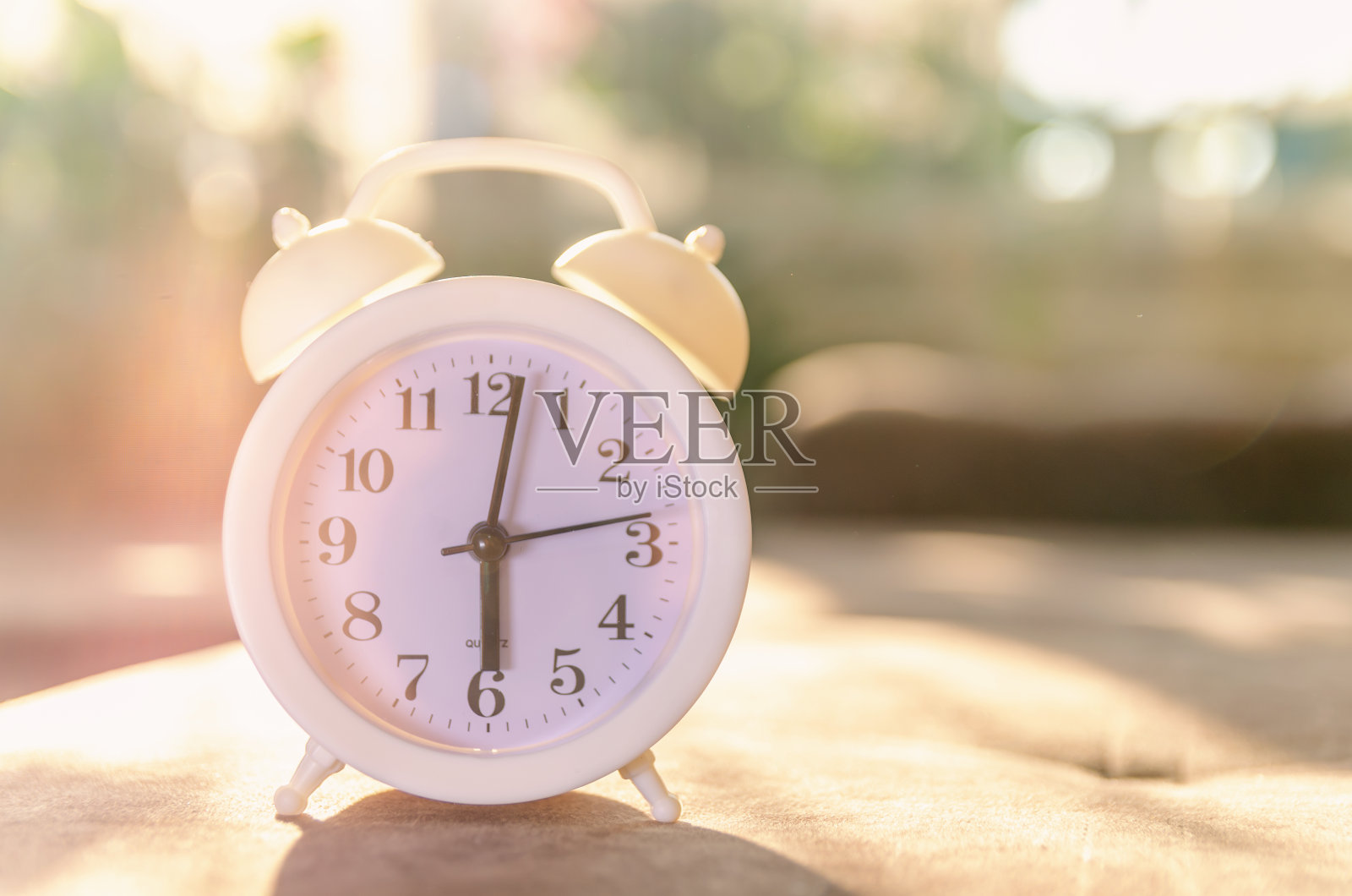 阳光下的沙发上放着一个白色的闹钟。美丽的背景与闹钟照片摄影图片