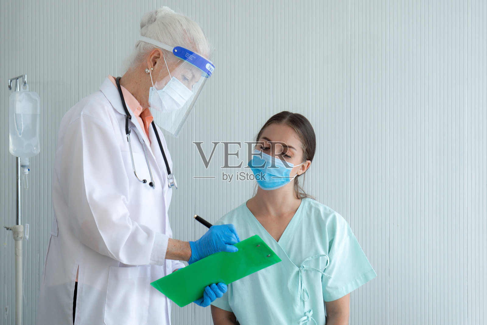 一位戴着面罩和防护面罩的老年医生向这位年轻病人解释了检查前的步骤。照片摄影图片