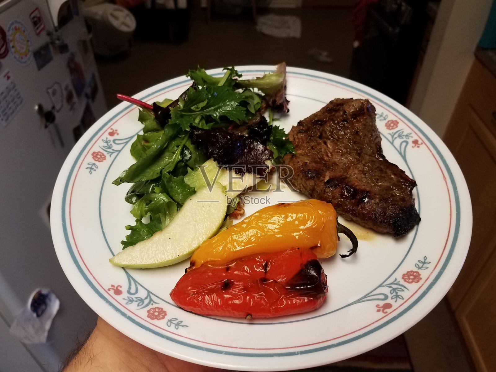 手里拿着一盘牛排、青椒和沙拉照片摄影图片