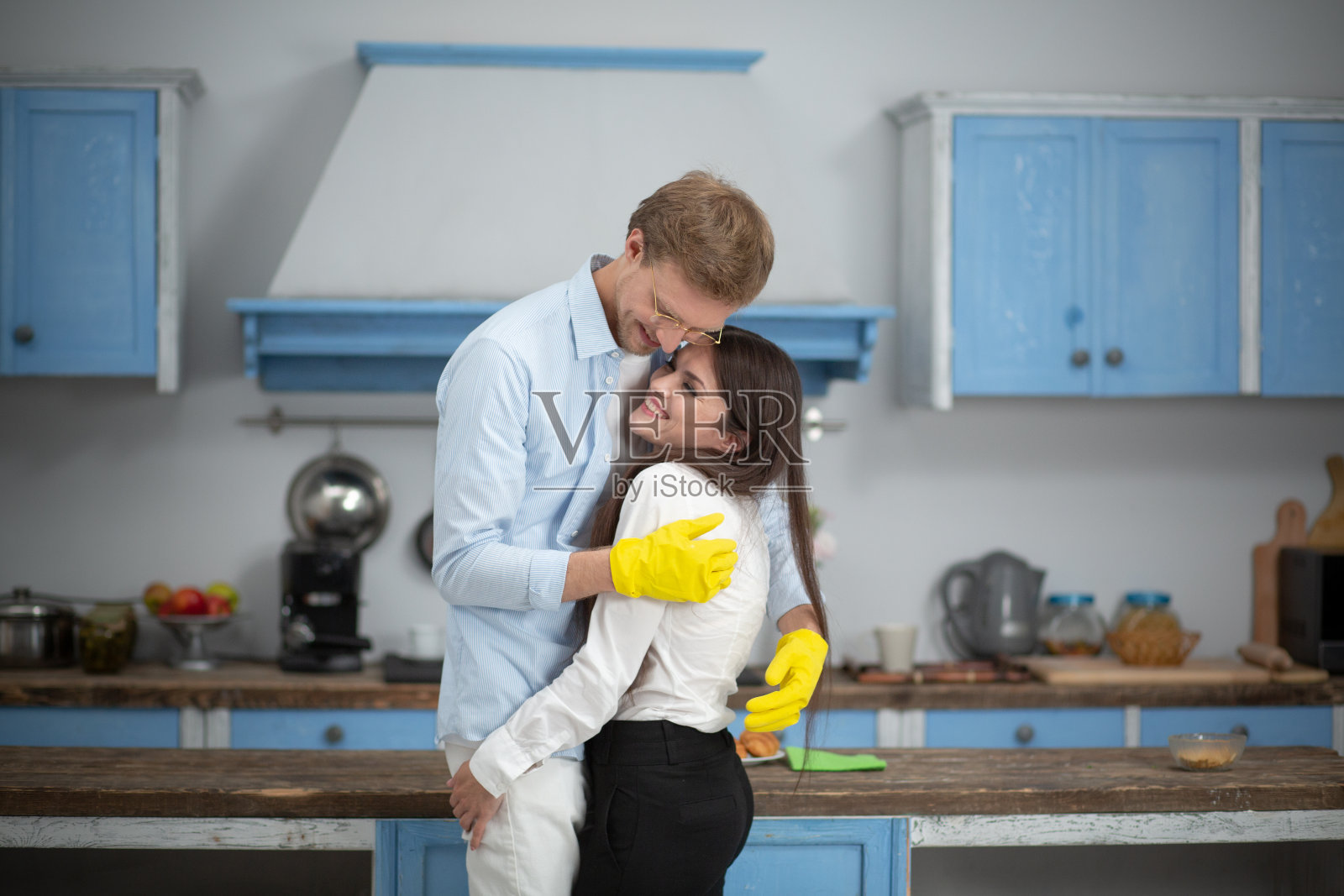 快乐的夫妇在厨房拥抱。快乐的男人穿着居家衣服，戴着黄色橡胶手套，在家做饭的时候拥抱着他的妻子照片摄影图片