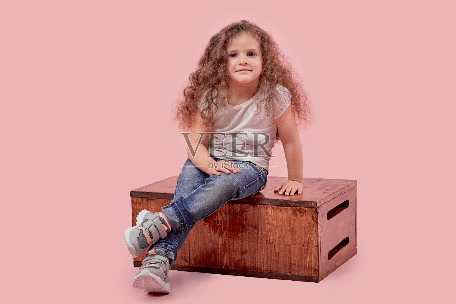 一个小孩坐在木架上，背景是空的。这个婴儿是金发的。照片摄影图片