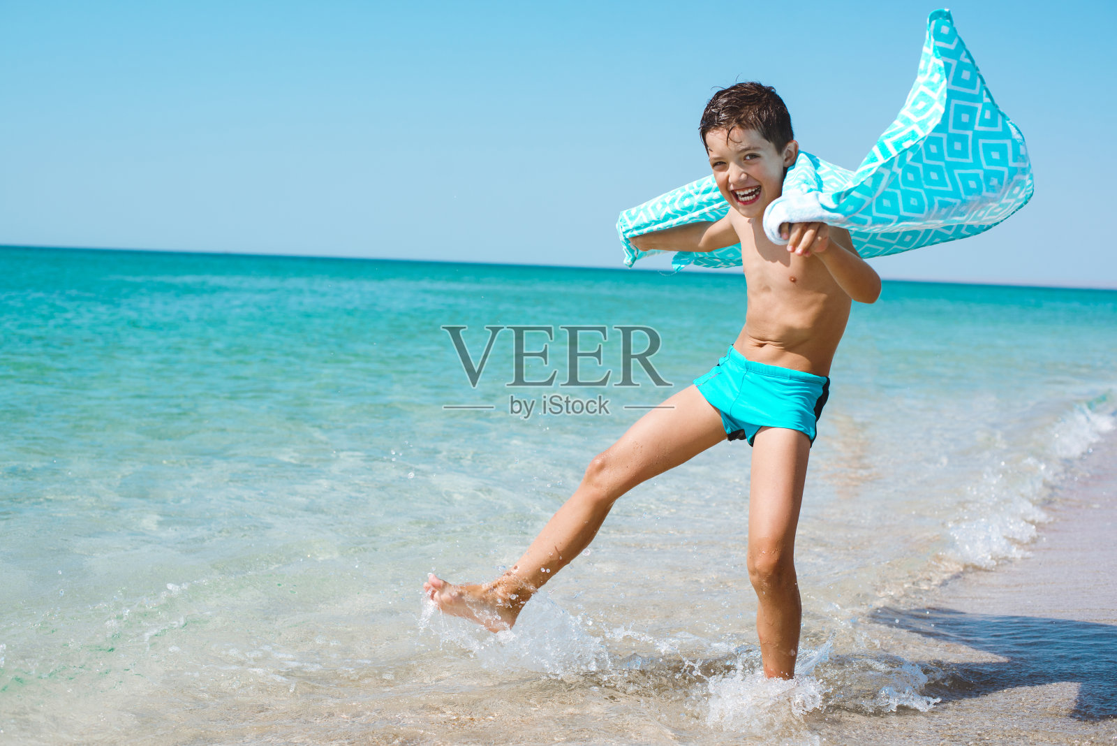 一个欢快的孩子在海滩上裹着一条鲜艳的沙滩浴巾。照片摄影图片