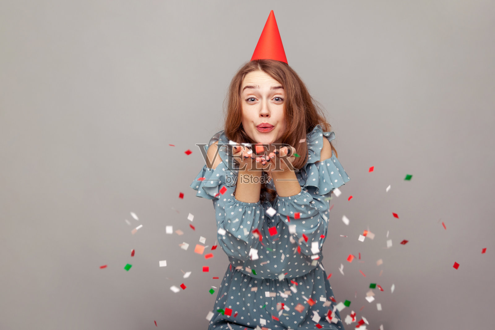 无忧无虑快乐的女孩穿着皱褶衬衫和滑稽的派对帽吹闪光，微笑着享受生日庆祝照片摄影图片