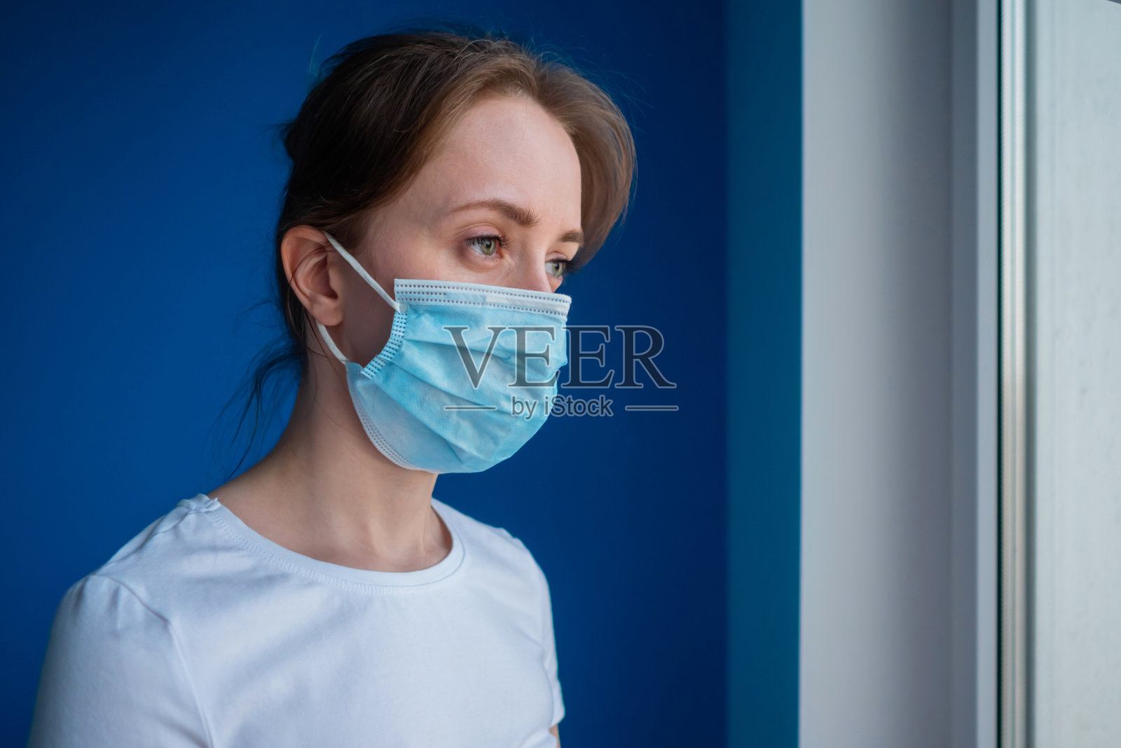 沉思的女人戴着医用口罩，看着窗外的景色照片摄影图片