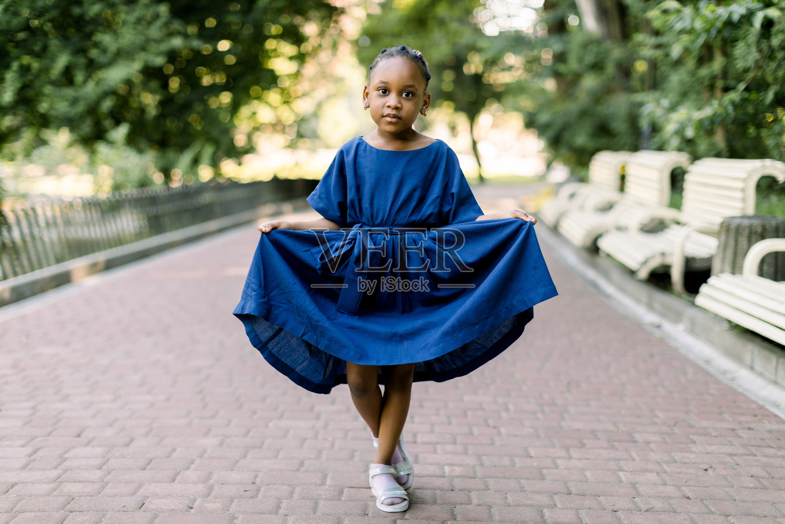 可爱又有趣的非洲小女孩穿着五颜六色的蓝色连衣裙微笑着站在公园小巷