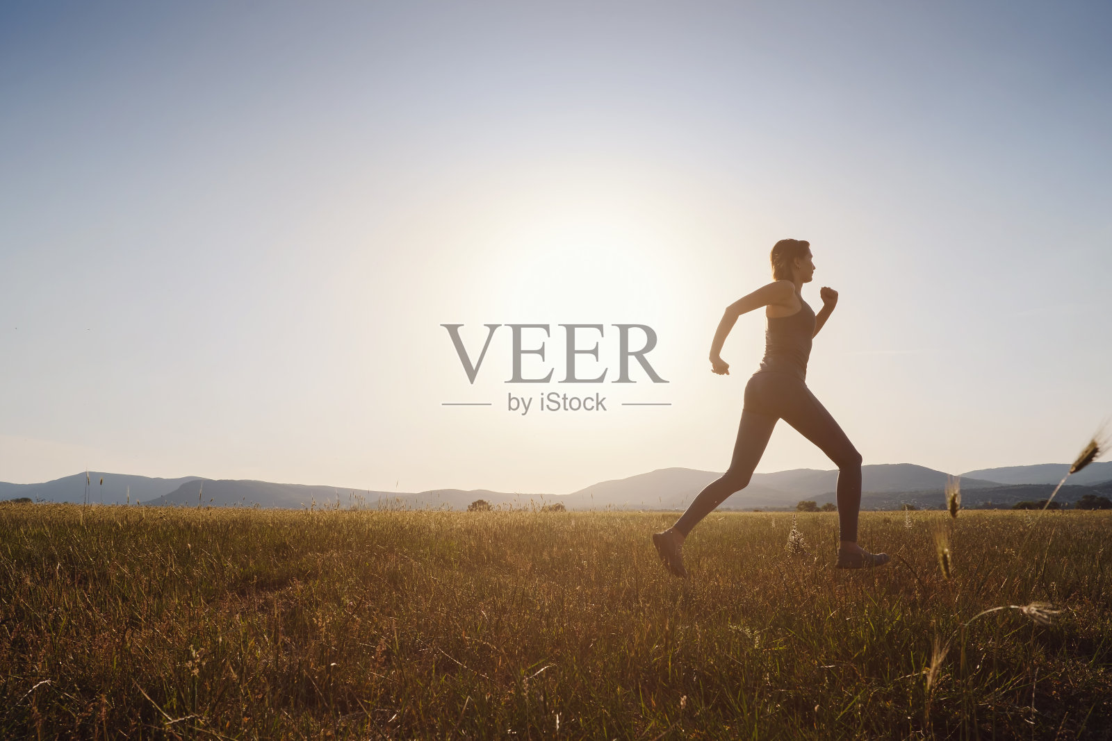 慢跑的女人在夏天的田野在日落照片摄影图片