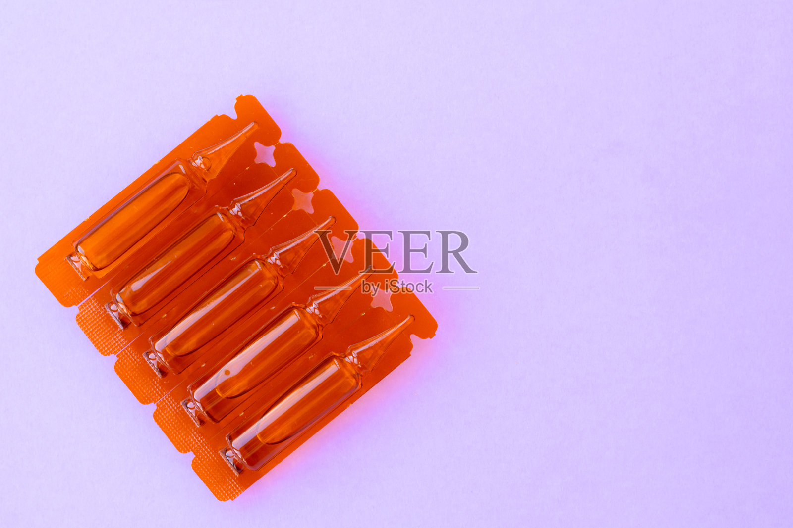 紫色背景的一角有注射用药物安瓿。透明胶囊，含液体保健药。制药行业。照片摄影图片