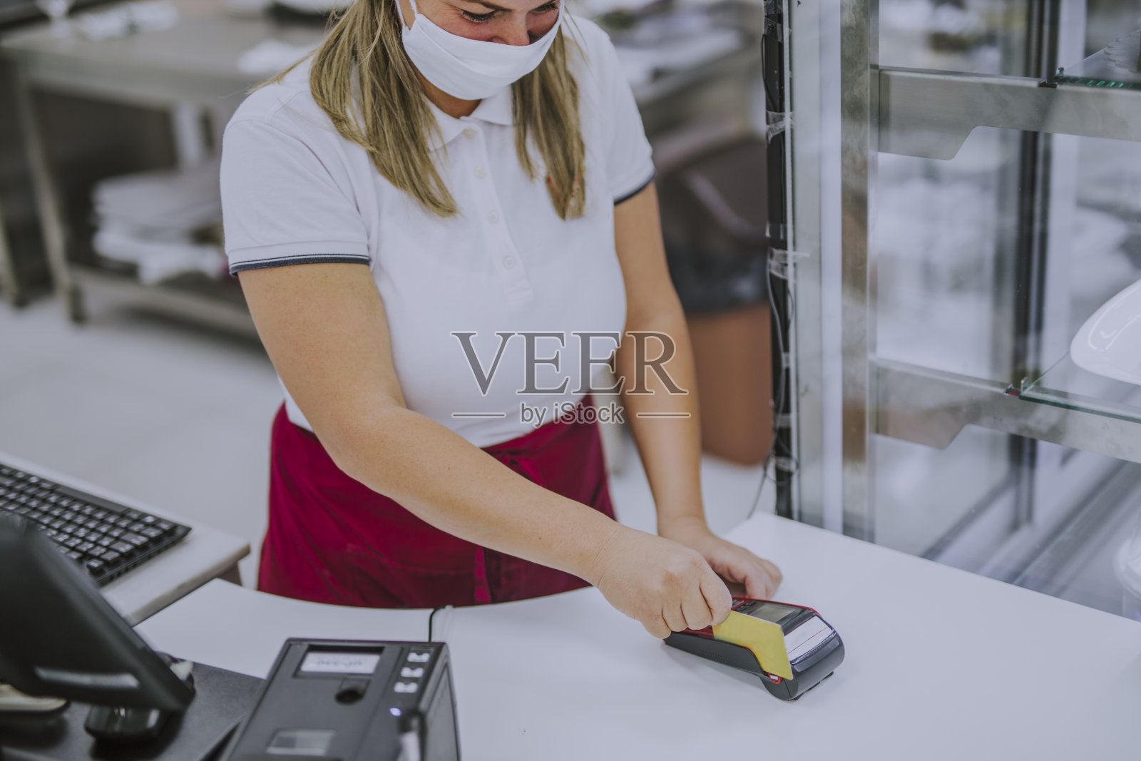 年轻的成年人和友善的女收银员面带微笑，笑容满面地站在超市收银台后面，在疫情期间戴着口罩照片摄影图片