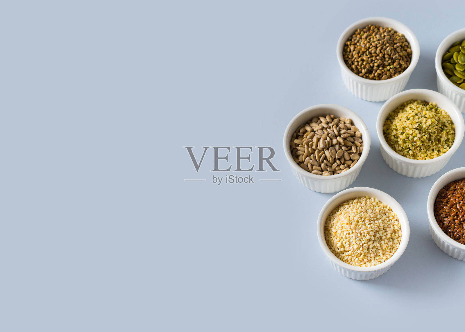 不同的种子-大麻，芝麻，葵花籽和南瓜籽在小碗俯视图在蓝色背景照片摄影图片