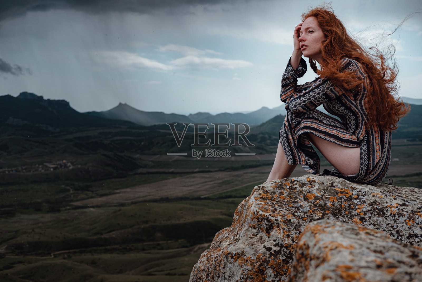 金格女人坐在悬崖上，看着即将来临的暴风雨照片摄影图片