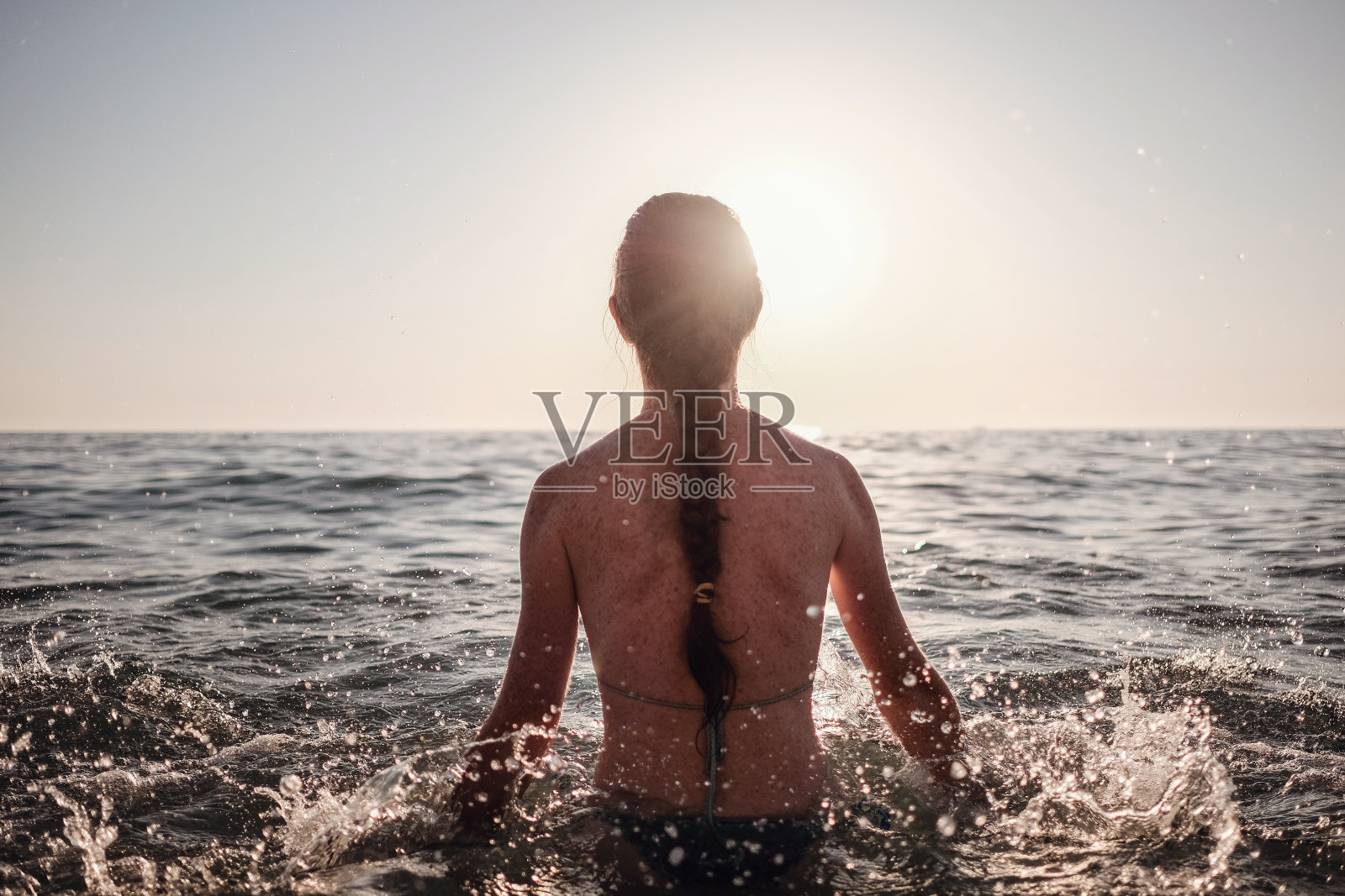 美丽的模特女孩在夕阳下在大海中溅起水花照片摄影图片