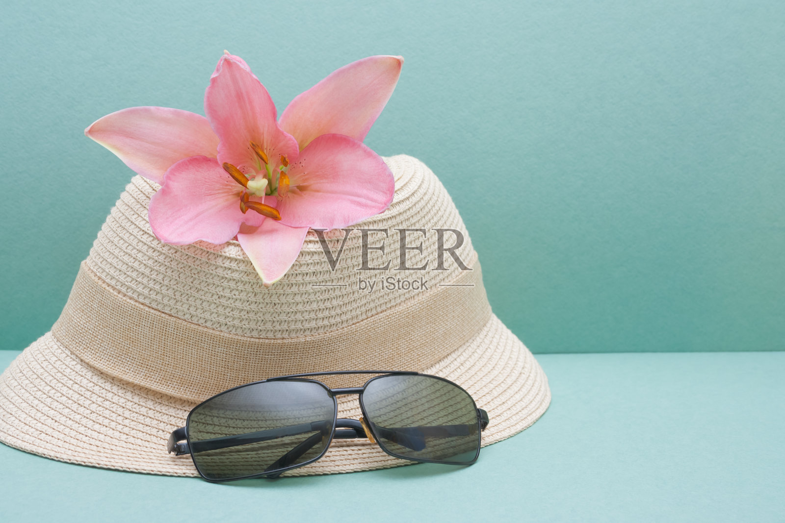 在度假胜地度过暑假的概念。巴拿马，太阳镜和粉红色的百合花在绿松石背景照片摄影图片