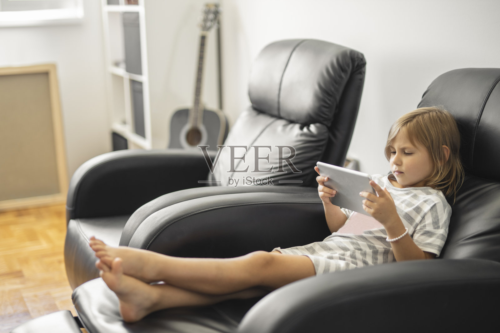 穿着睡衣坐在扶手椅上使用平板电脑的焦虑小女孩照片摄影图片