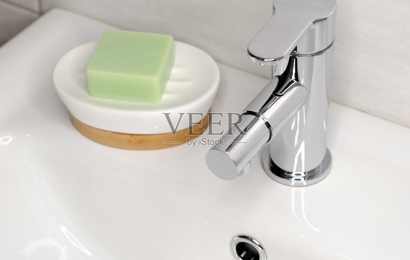 在浴室里的一个白色水槽里，放着一个肥皂盘，旁边是一个镀铬的水龙头。照片摄影图片