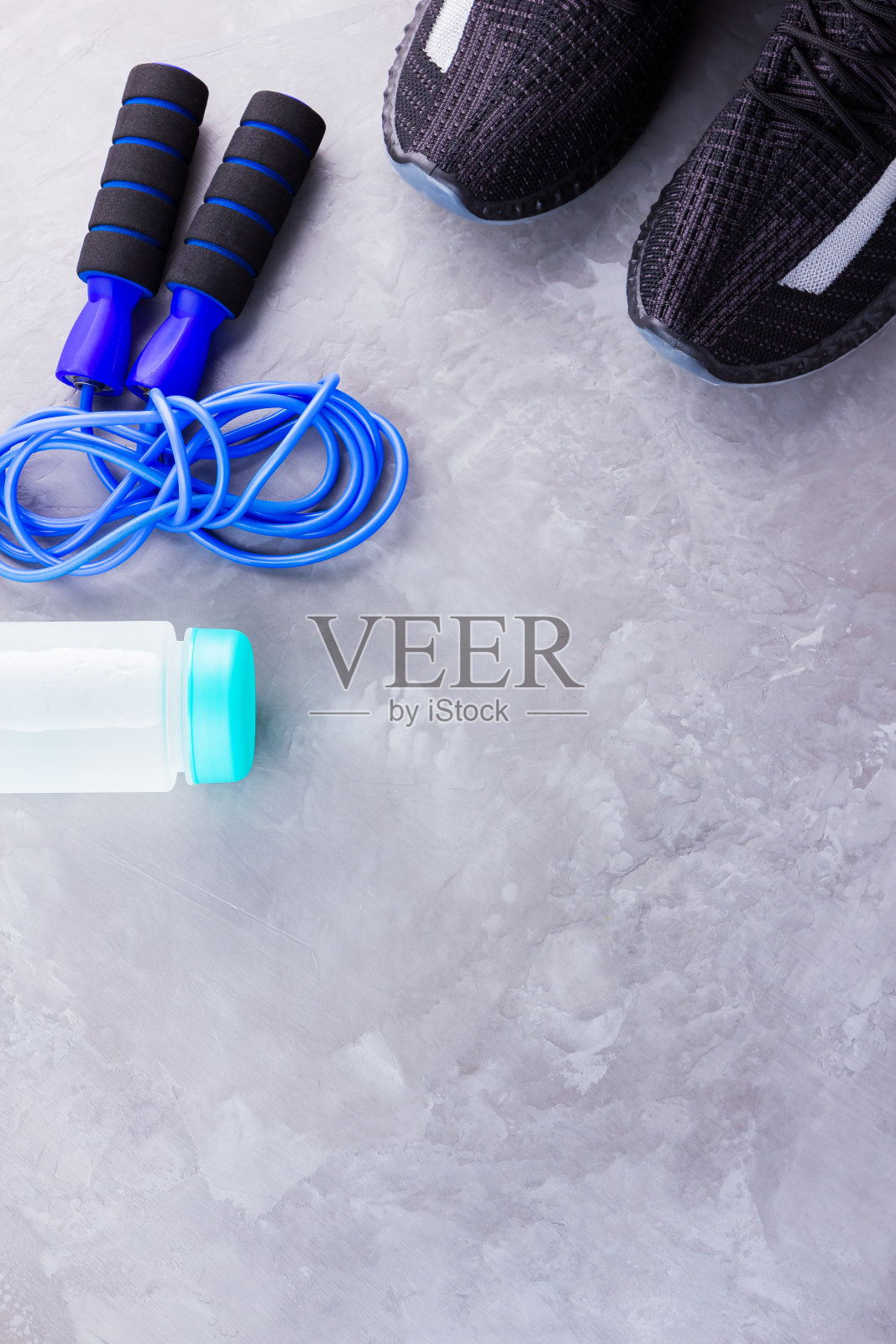 健身概念运动鞋，跳绳和一瓶水。灰色背景上的运动器材。健康的生活方式的概念。副本的空间。俯视图照片摄影图片