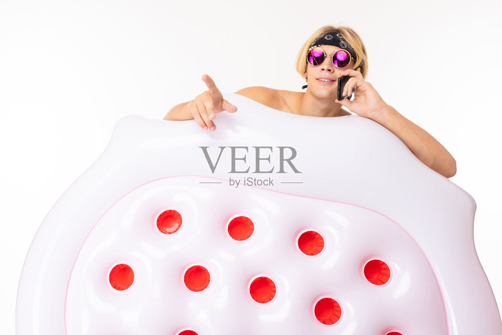 年轻的白人金发男子站在泳衣与大橡胶沙滩床垫打电话电话孤立在白色的背景照片摄影图片