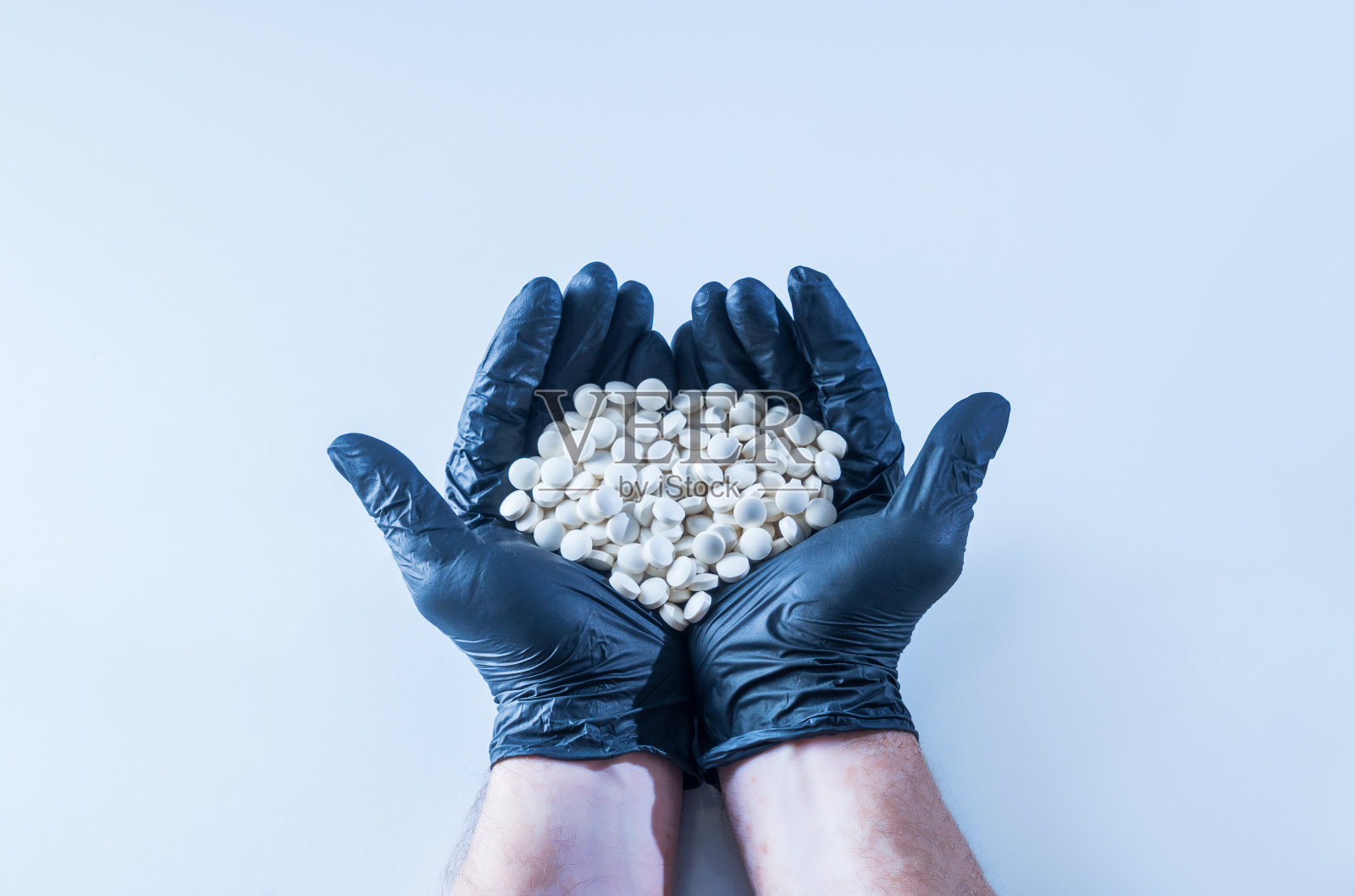 双手拿着白色药丸，戴着黑色乳胶手套。健康和预防的概念。照片摄影图片