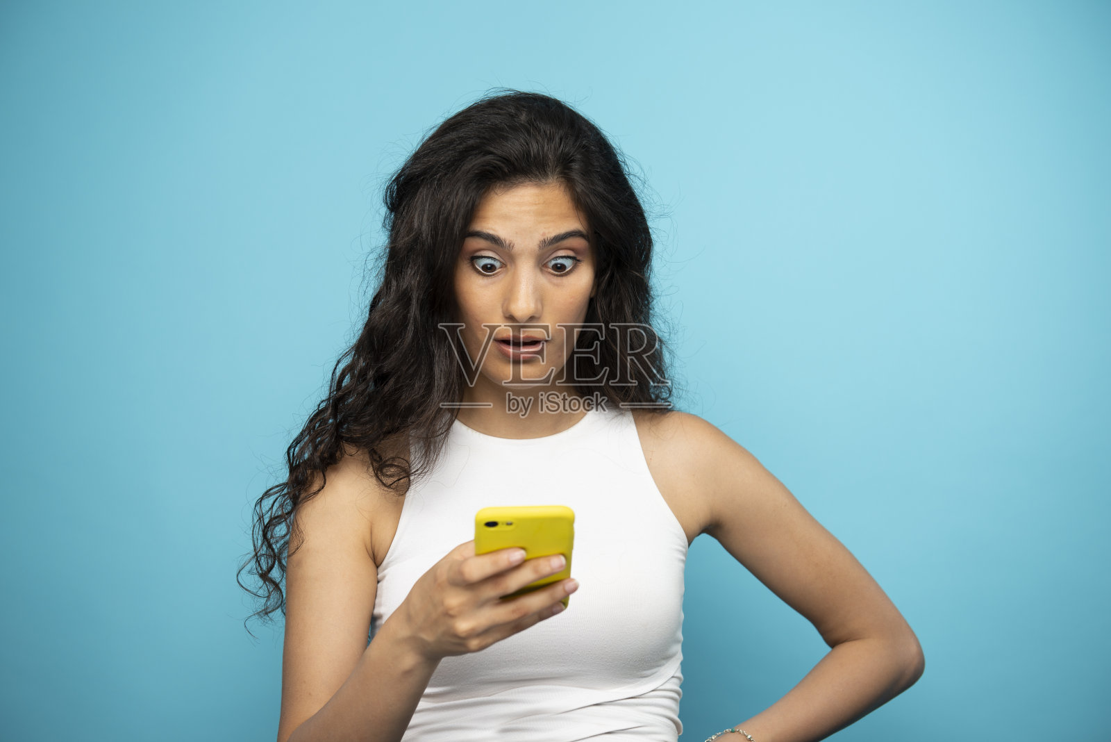 年轻的女孩盯着手机看，很吃惊。照片摄影图片