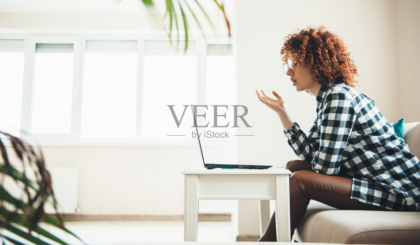 可爱的白人女人，卷头发，戴眼镜，在笔记本电脑上解释一些在线会议照片摄影图片