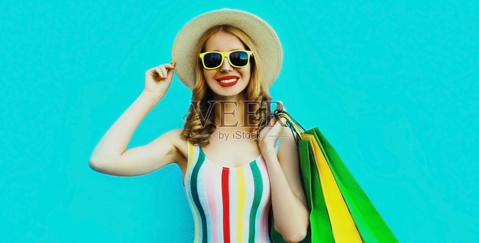 微笑的年轻女子肖像购物袋在彩色条纹t恤，夏季圆帽在蓝色的背景照片摄影图片