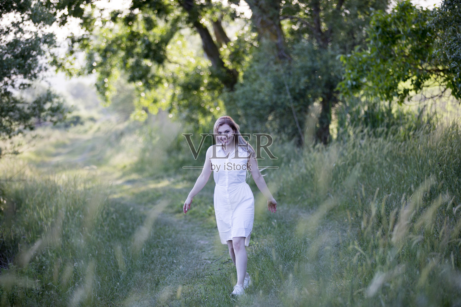 在一个阳光明媚的日子里，一个年轻女子在草地上伸出双手照片摄影图片