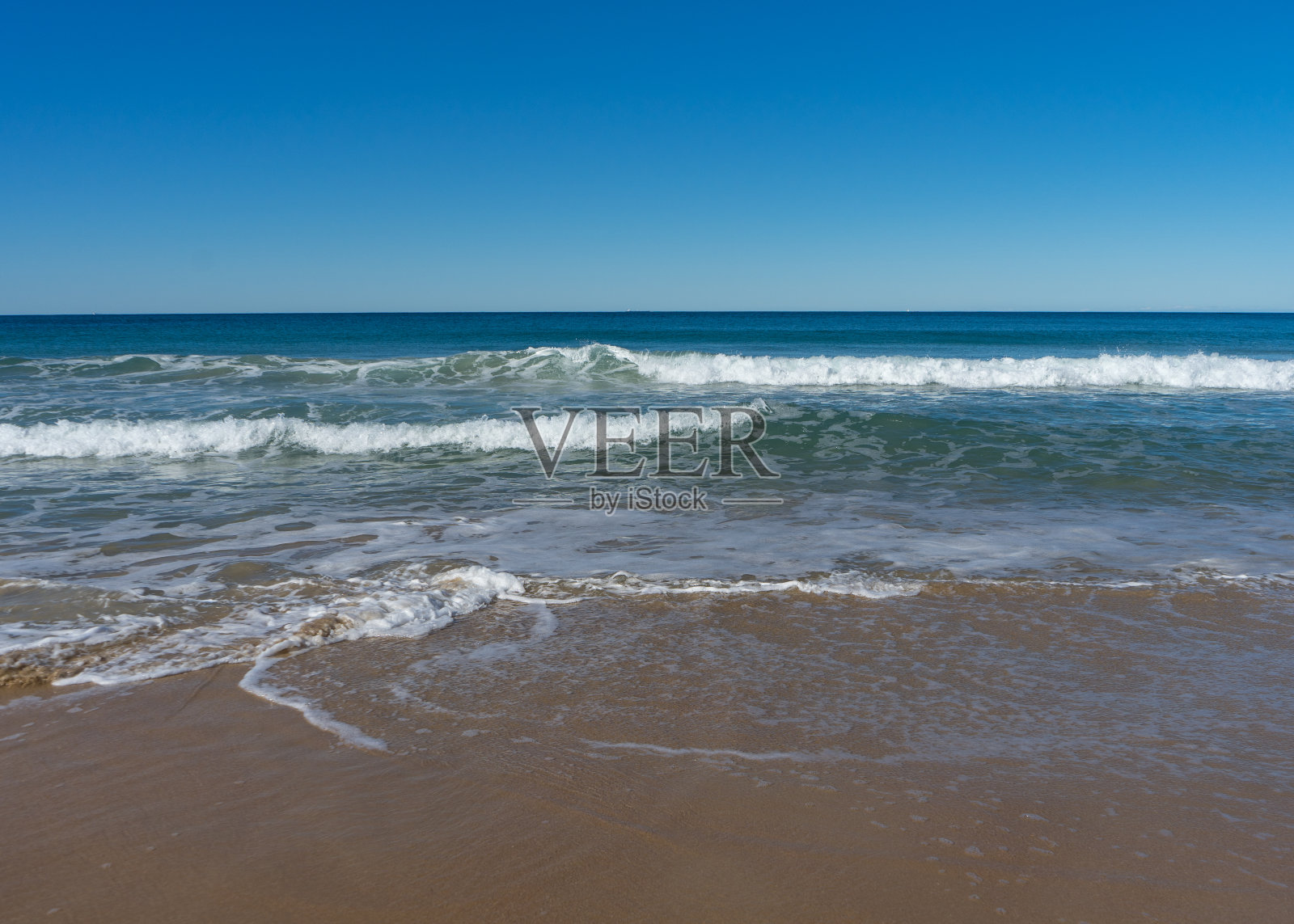 低角度的照片，海浪打破了一个海滩与蓝天的背景照片摄影图片