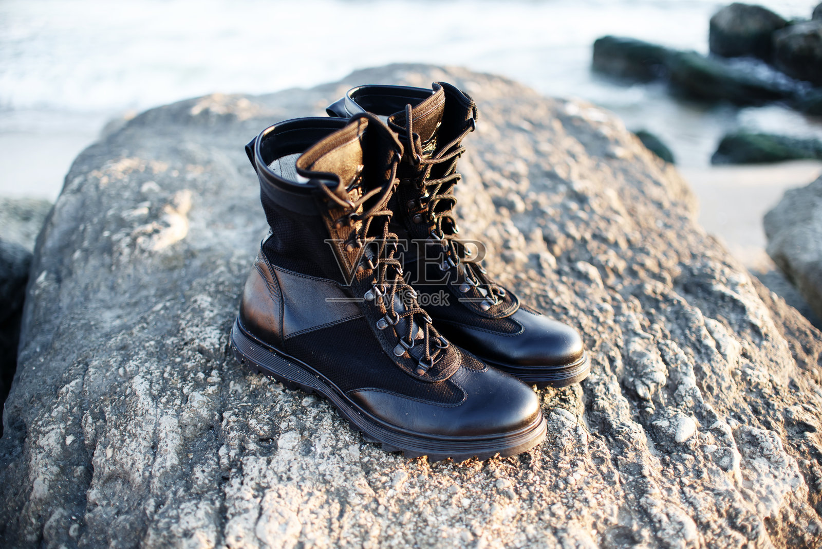 在石头和大海的背景下进行户外活动的男子军队黑色靴子与皮革和织物鞋带照片摄影图片