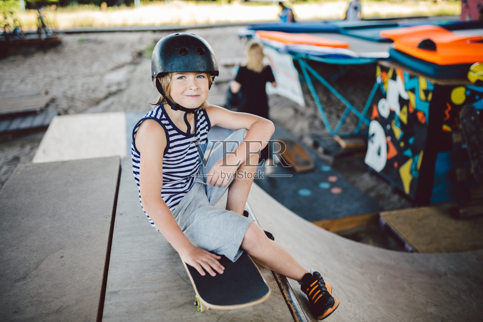 时髦的滑板者享受自由时间在滑板公园，坐在半管坡道。滑冰后休息。男孩在操场上用滑板放松。孩子坐在坡道上，等着他的朋友照片摄影图片