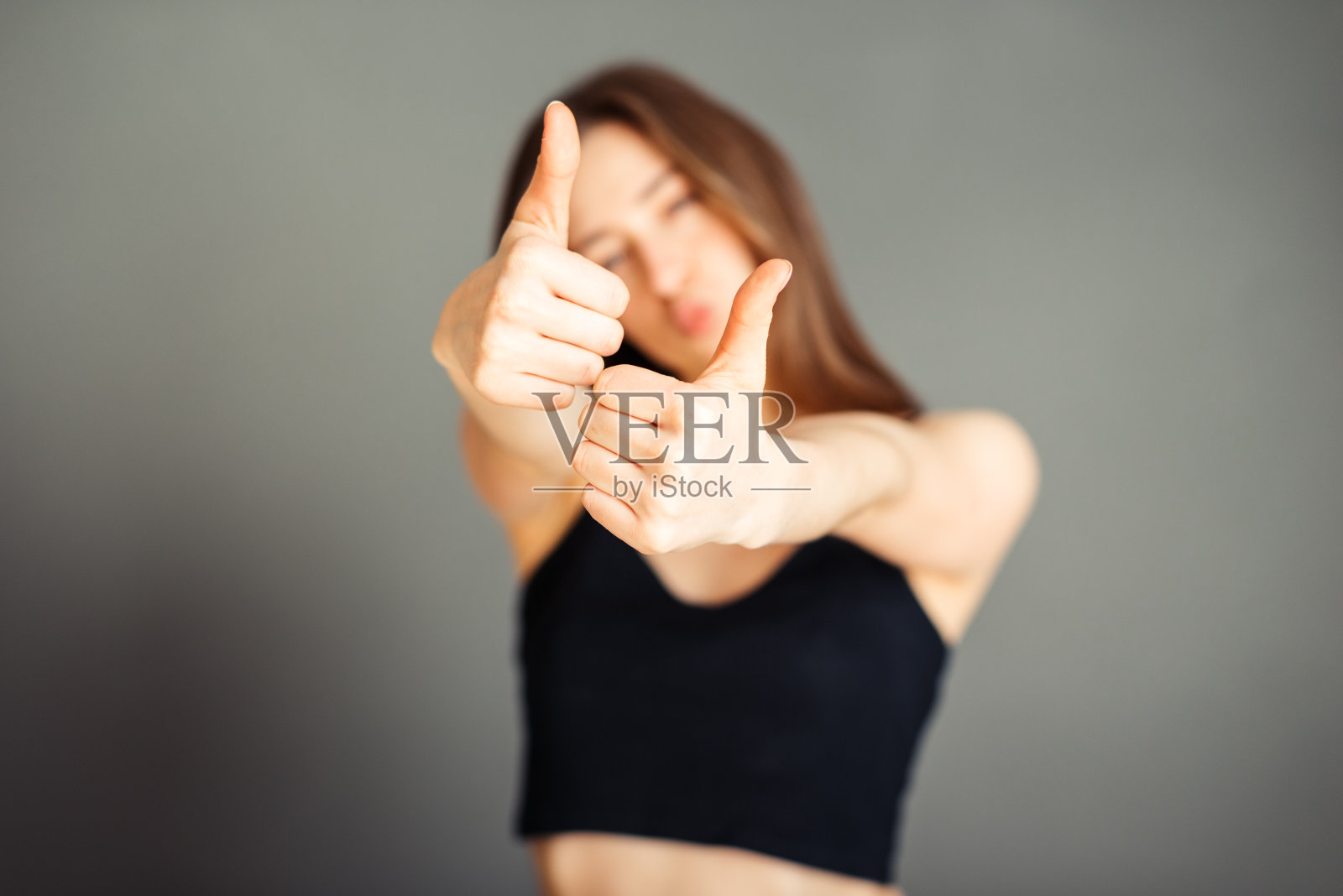 穿着黑色上衣的女孩，拇指向上翘着。在一个灰色的背景。没有化妆，没有修饰。照片摄影图片