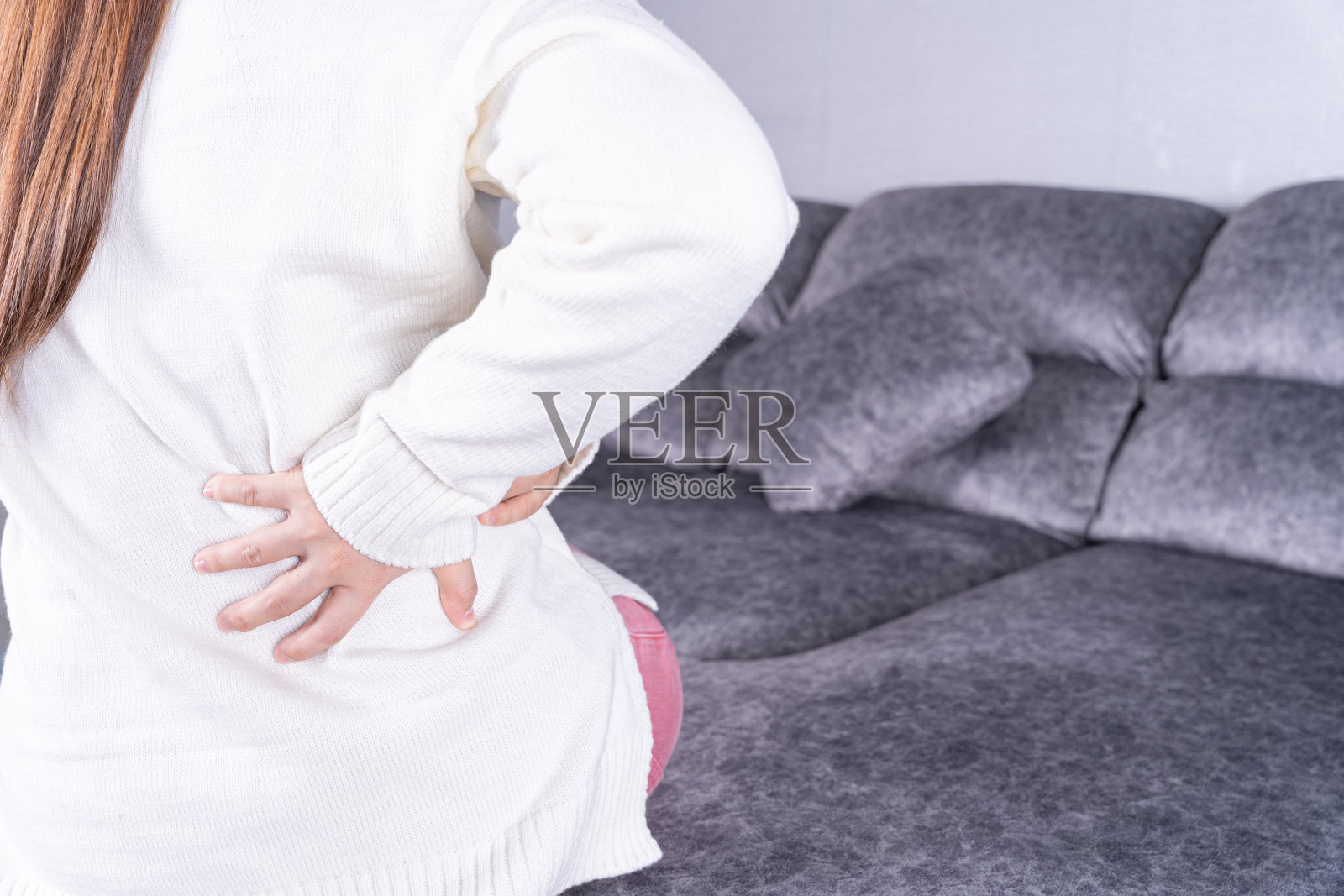 一名年轻女子坐在家里的沙发上时背部疼痛。医疗保健或日常生活概念。照片摄影图片