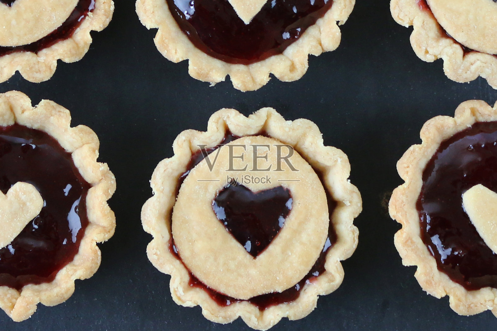 近距离图像的六排自制，酥皮糕点，树莓果酱挞与心形设计糕点顶部，在石板背景，升高的观点照片摄影图片